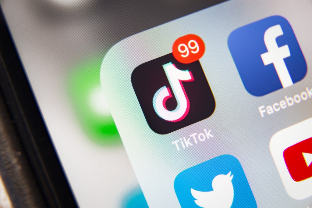 Close-up of a smartphone screen displaying the TikTok app icon with a notification badge showing 99 messages, alongside other social media app icons.