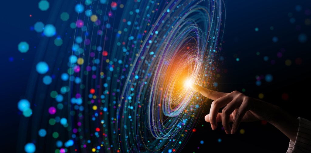 A close-up of a hand reaching out to touch a glowing point in a swirling, colorful cosmic vortex, symbolizing exploration and connection in space.