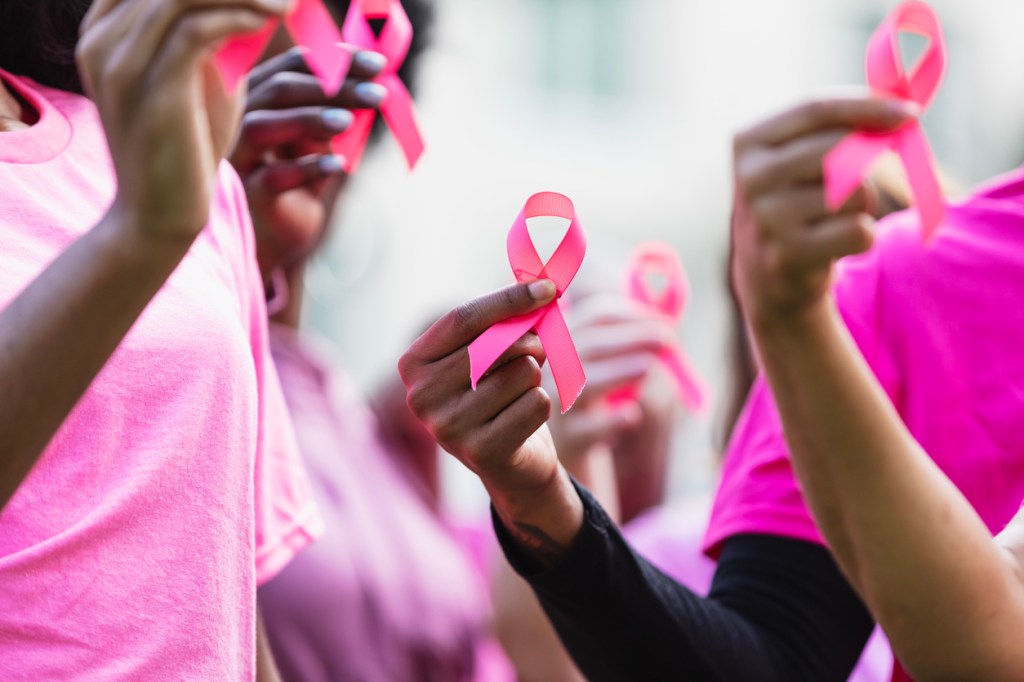 Participants wearing pink shirts hold pink awareness ribbons during a Breast Cancer Awareness event.