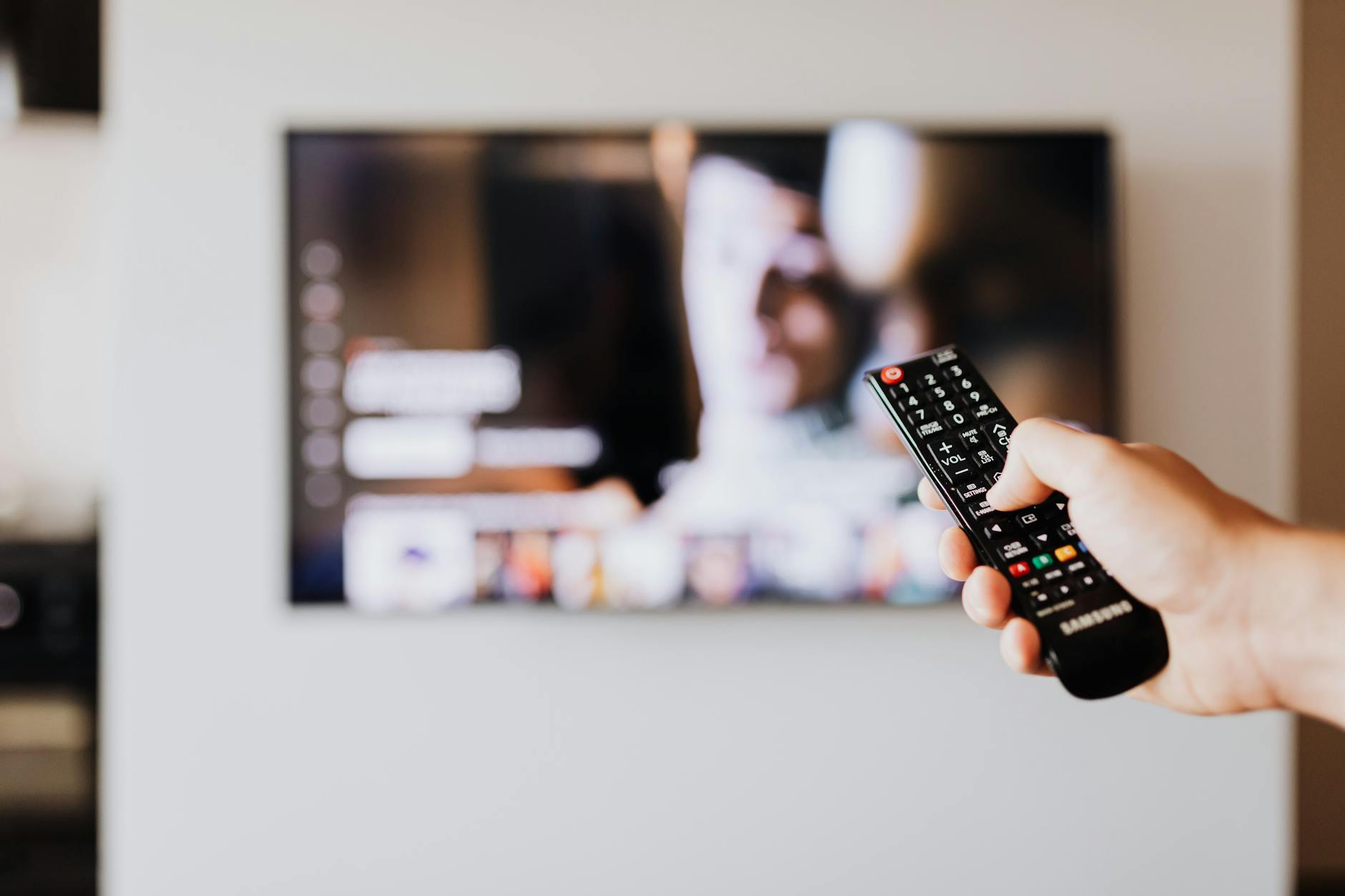 A person's hand holding a remote control aimed at a television displaying a show screen.